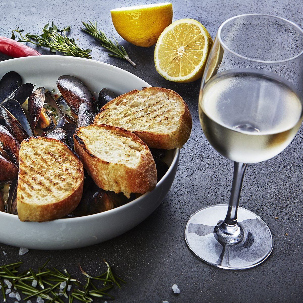 mussels in white wine sauce with glass of white wine white bread toasts