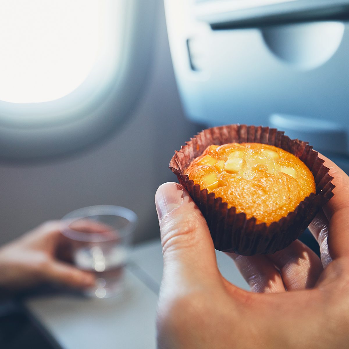 Comfortable traveling by airplane. Passenger is holding muffin and cup with water during the flight.; Shutterstock ID 764496220