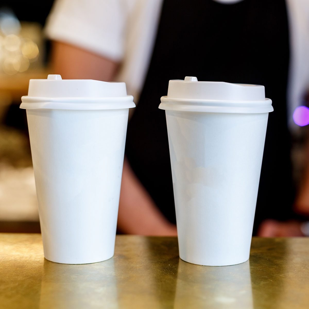 Barista making two cappuccinos in a paper cup to go, cups on a counter