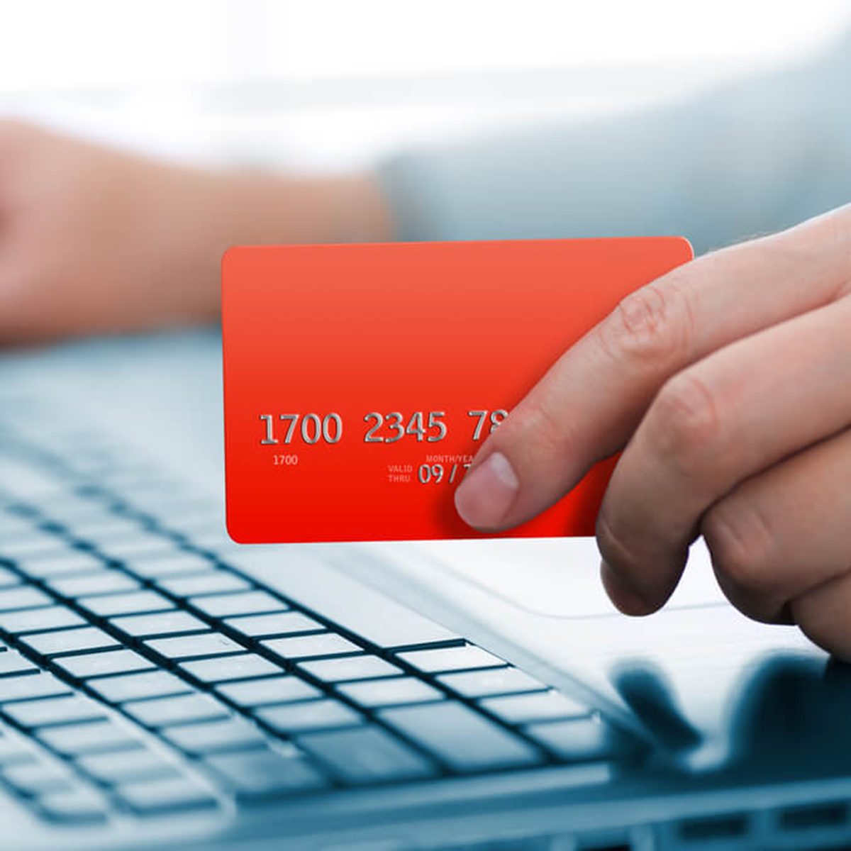 Man holding credit card in hand and entering security code using laptop keyboard