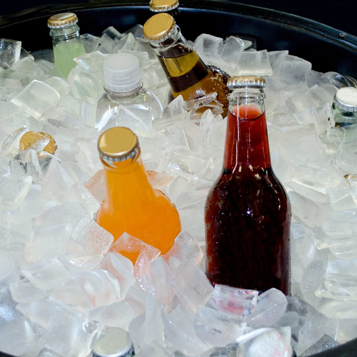 bottles of various kinds of soda chill in a large in of crushed ice