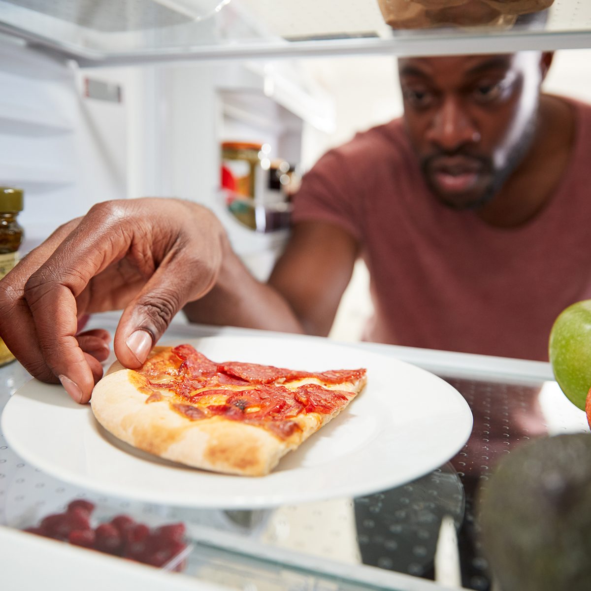 View Looking Out From Inside Of Refrigerator As Man Opens Door For Leftover Takeaway Pizza Slice