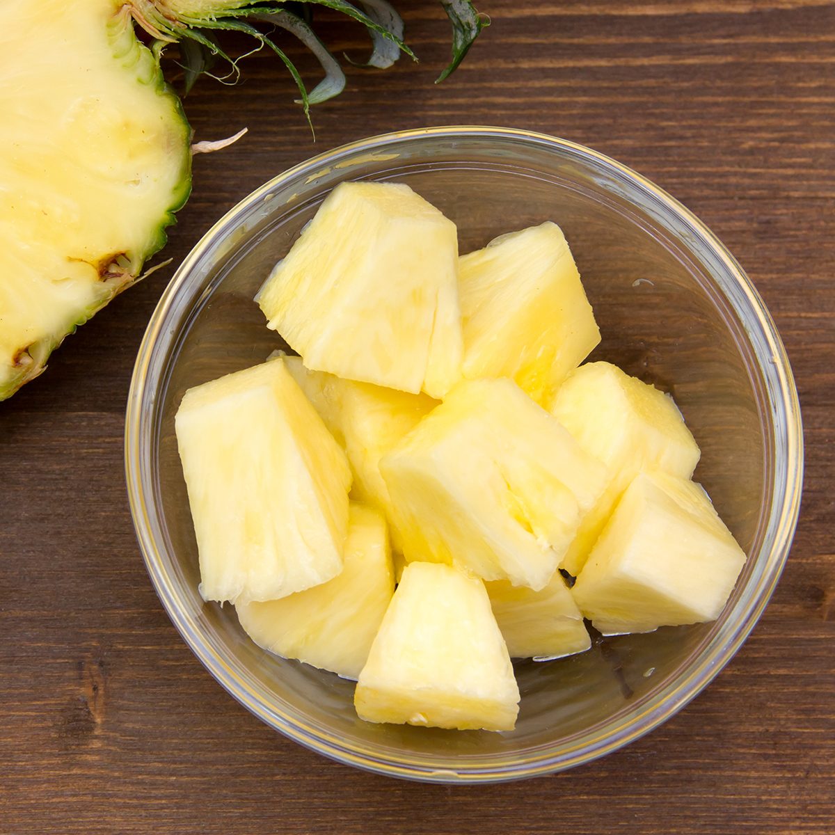 Pineapple cubes on bowl on wooden table seen from above