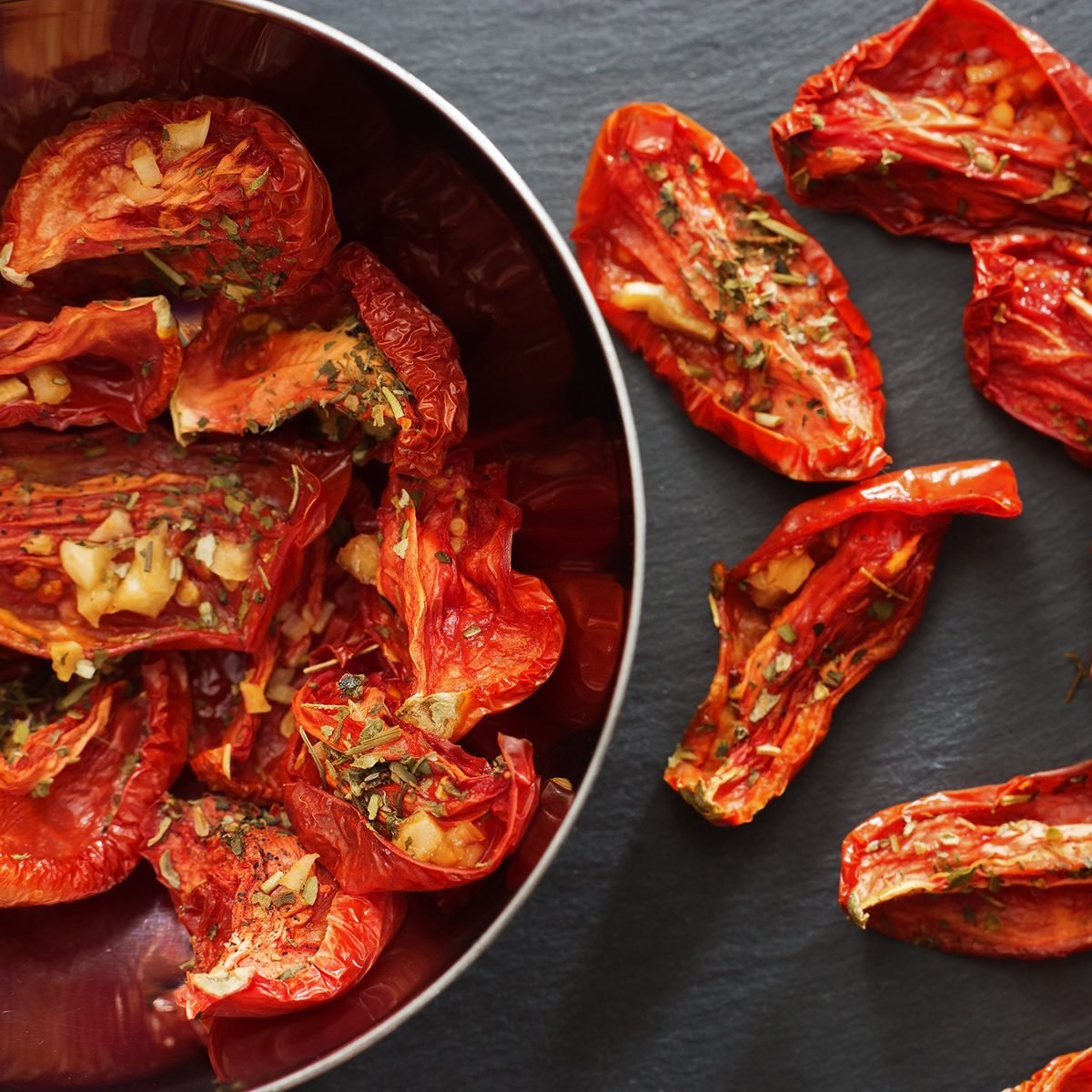 Tomatoes sun-dried in small pieces lying in a metal dish on a dark background.