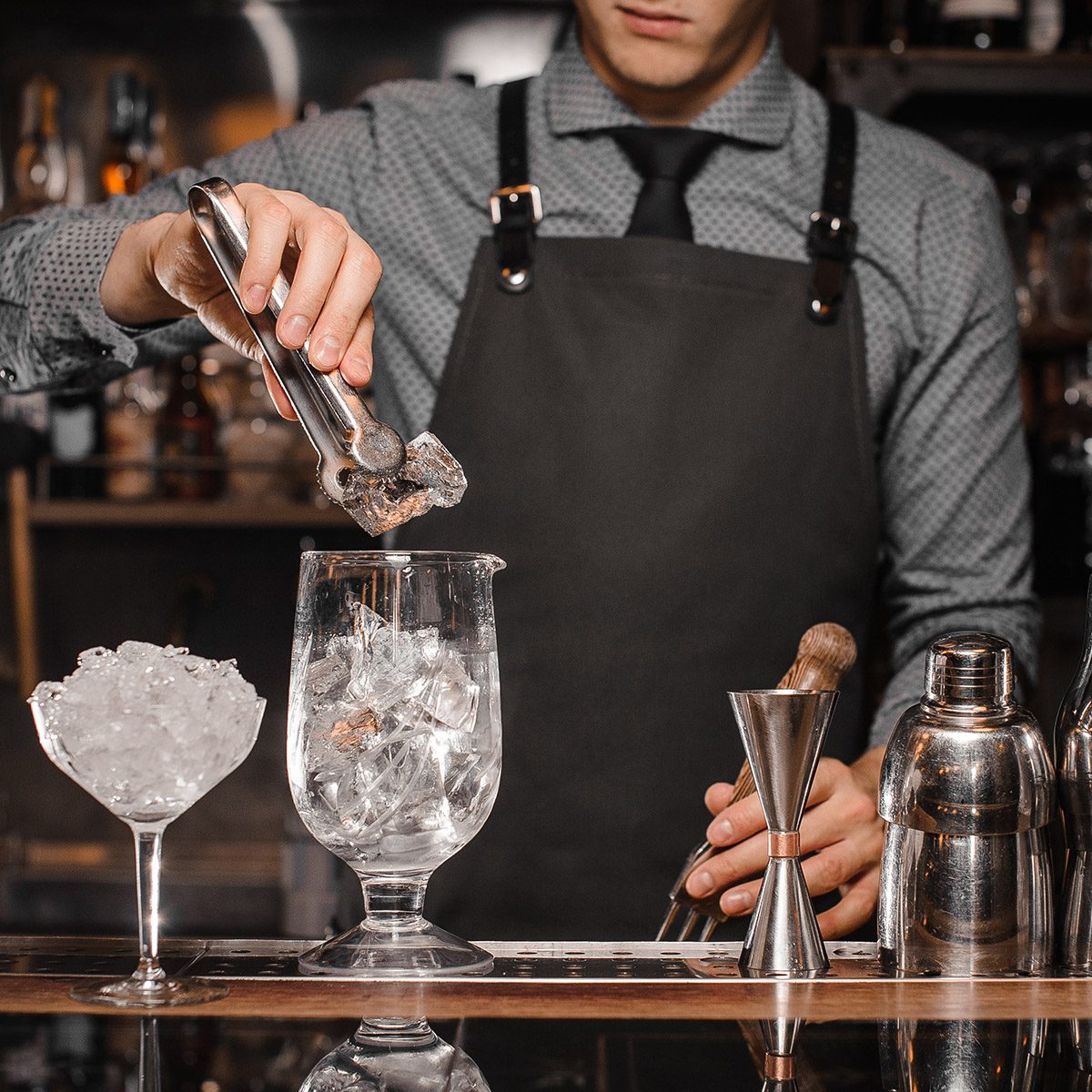 Bartender making a cocktail with help of the bar equipment arranged on the bar counter