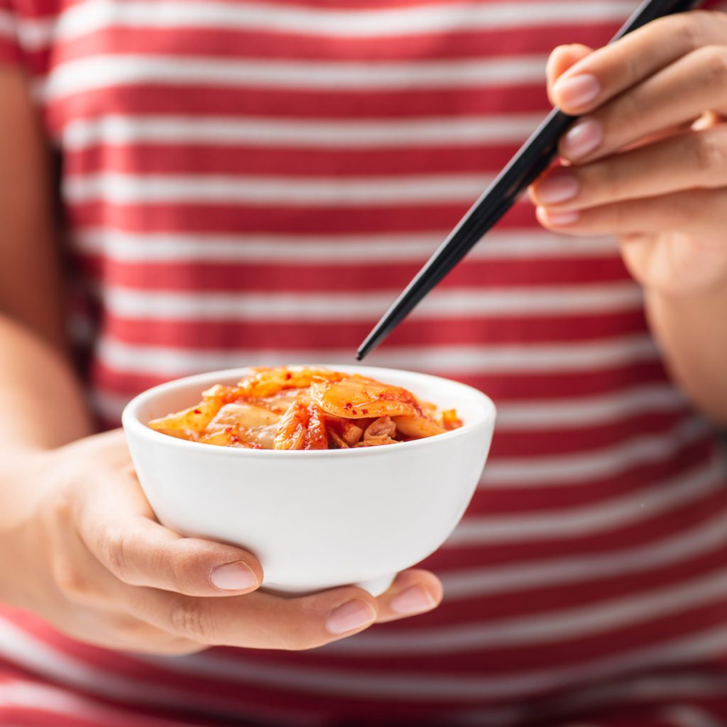 Woman holding chopsticks for eating kimchi cabbage in a bowl, Korean food; Shutterstock ID 1147372565; Job (TFH, TOH, RD, BNB, CWM, CM): Taste of Home