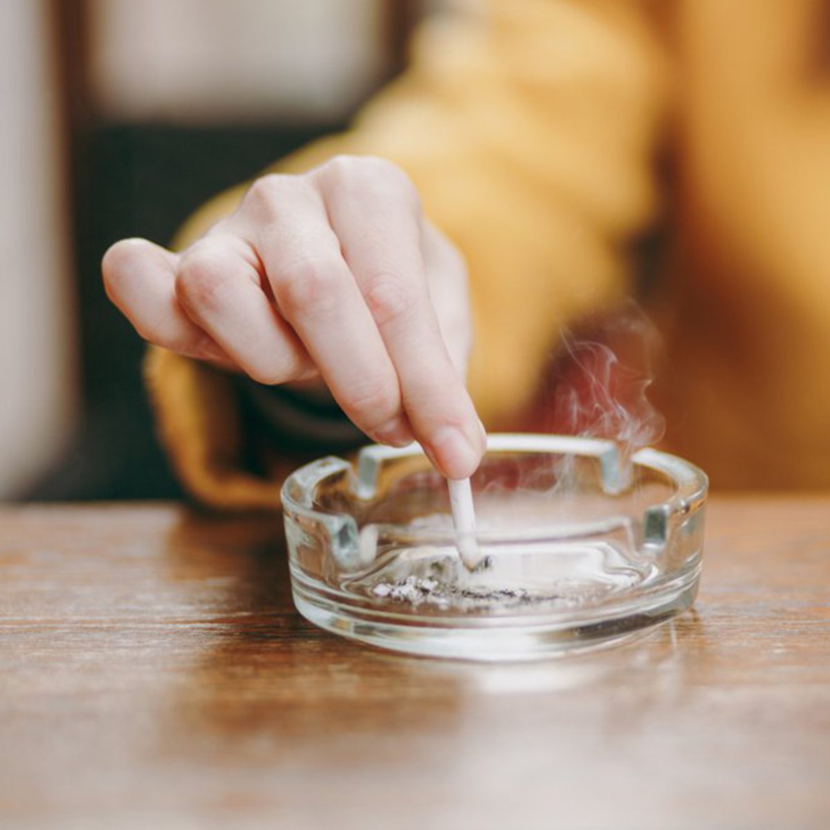 Focus on caucasian young woman hand putting out cigarette on glass ashtray on wooden table, cigarette butt, smoking is dying. Quit smoking. Health concept. Close up photo