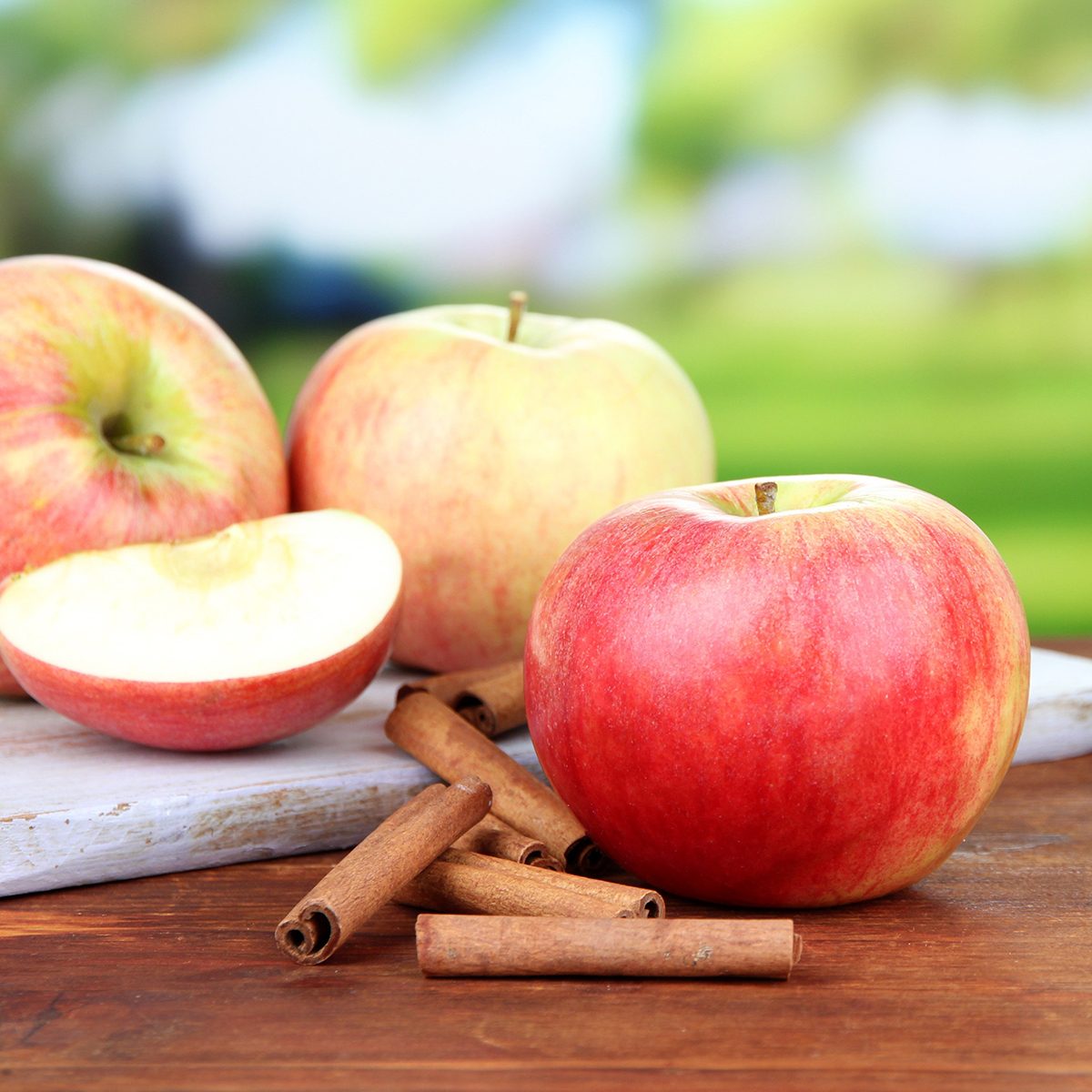 Ripe apples with cinnamon sticks on wooden table, on bright background