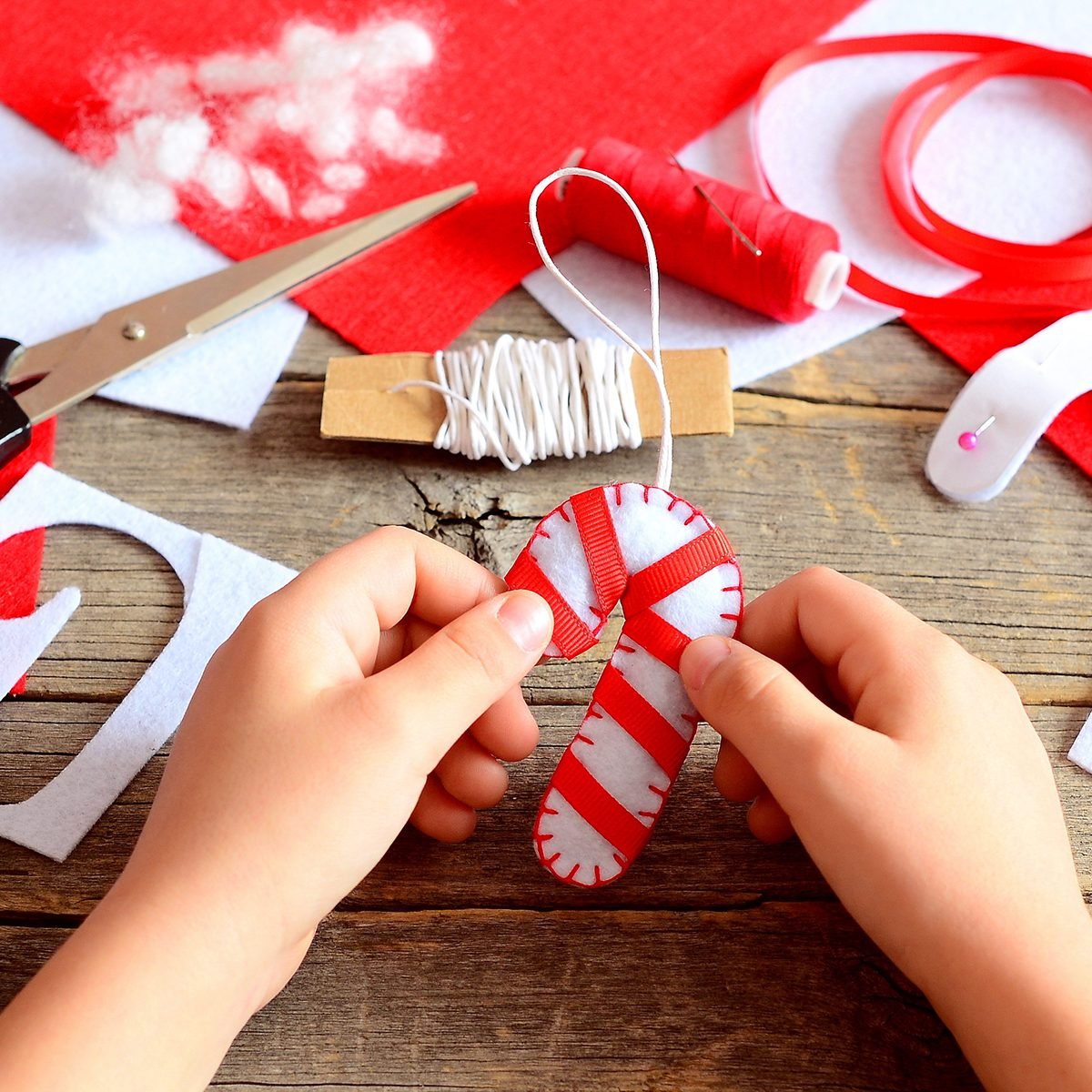 Child holds Christmas felt candy cane in his hands. Materials and tools to create Christmas tree decorations.