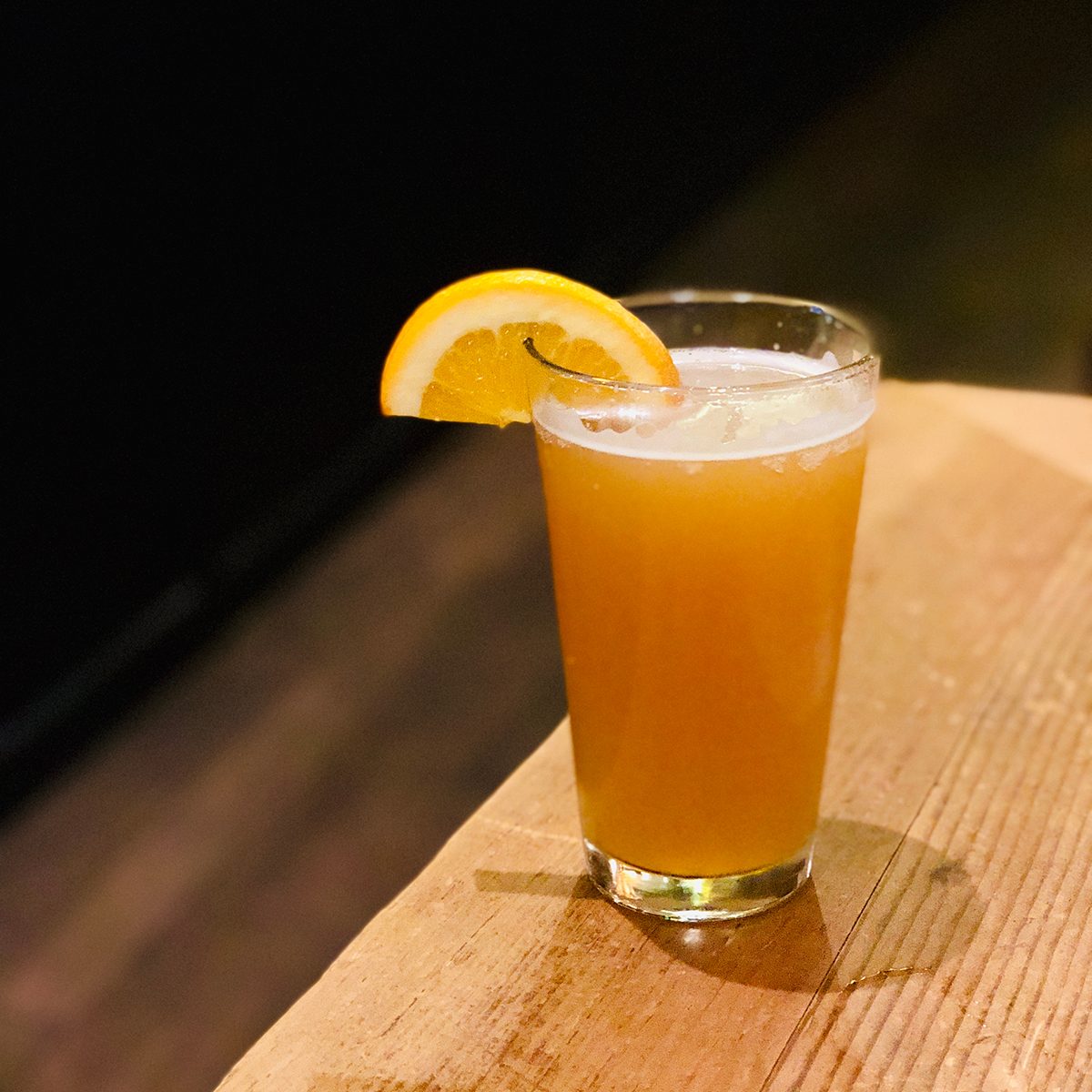 Craft Beer in Pint Glass with Orange Fruit Slice on Wooden Table