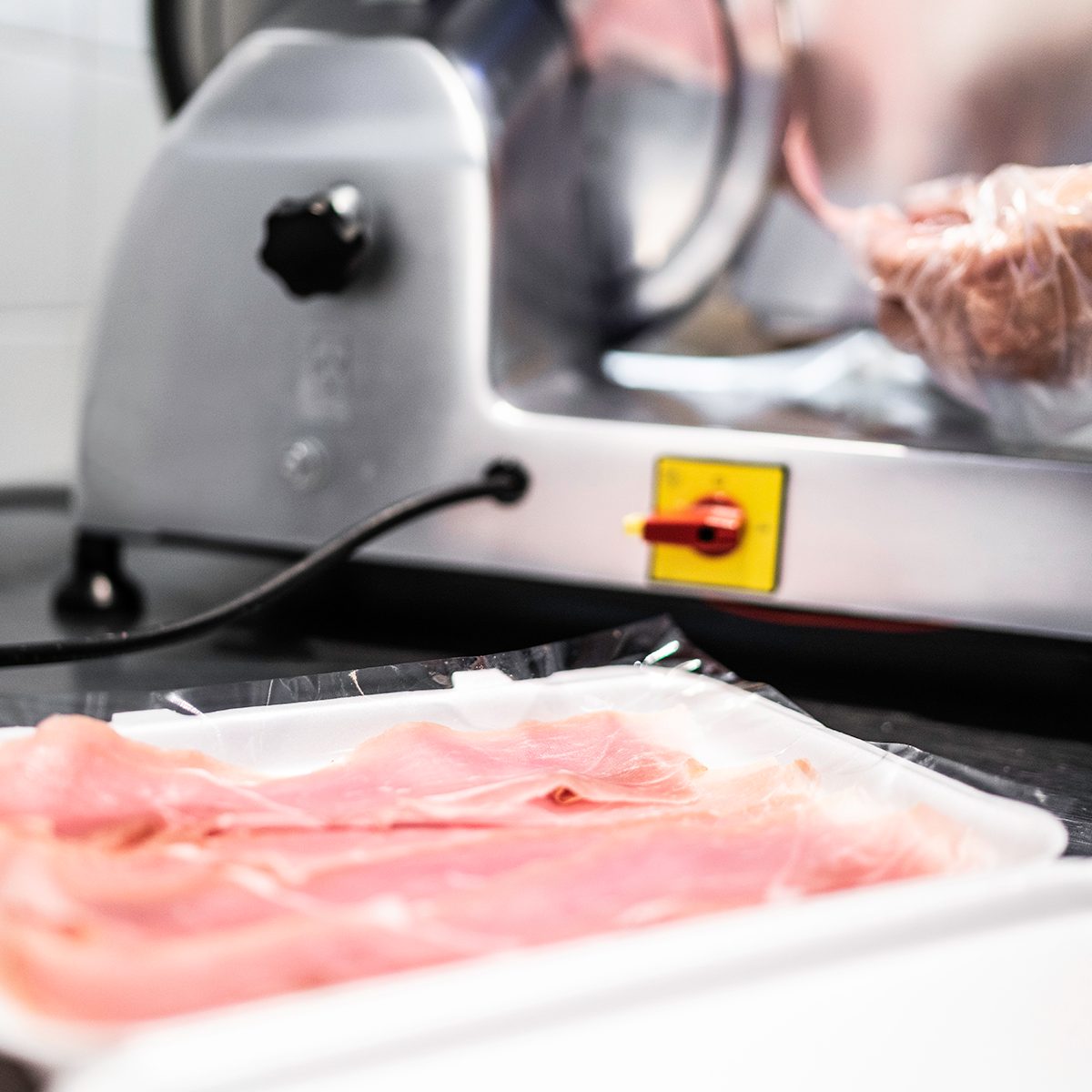 Human hand slicing a piece of ham in the meat slicer