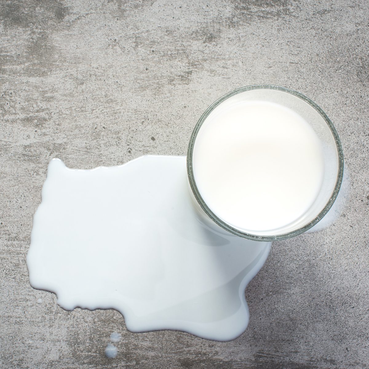 Spilt milk and a glass of milk on a gray concrete table