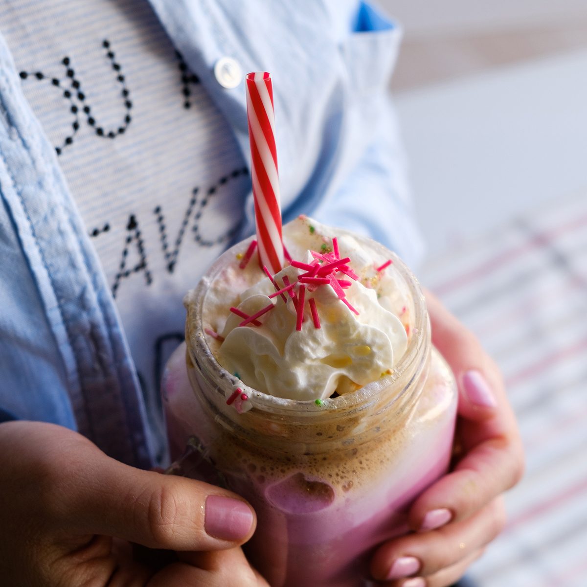 Girl is holding stylized mason jar cup of pink coffee with cream, marshmallow and decoration. Milk shake, cocktail. Unicorn coffee, unicorn food. Close up, soft focus
