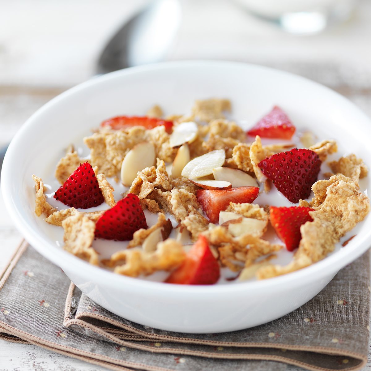 close up of a bowl of cereal and milk with almons and strawvberries on rustic wooden table