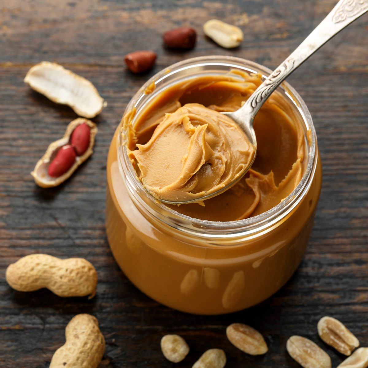 peanut paste in an open jar and peanuts in the peel scattered on the table