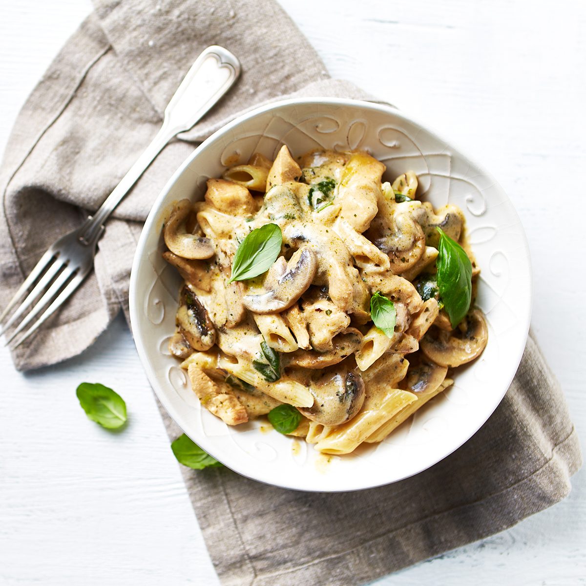 Penne pasta with mushrooms, chicken, spinach and cream sauce. Mediterranean cuisine. Flat lay. White background