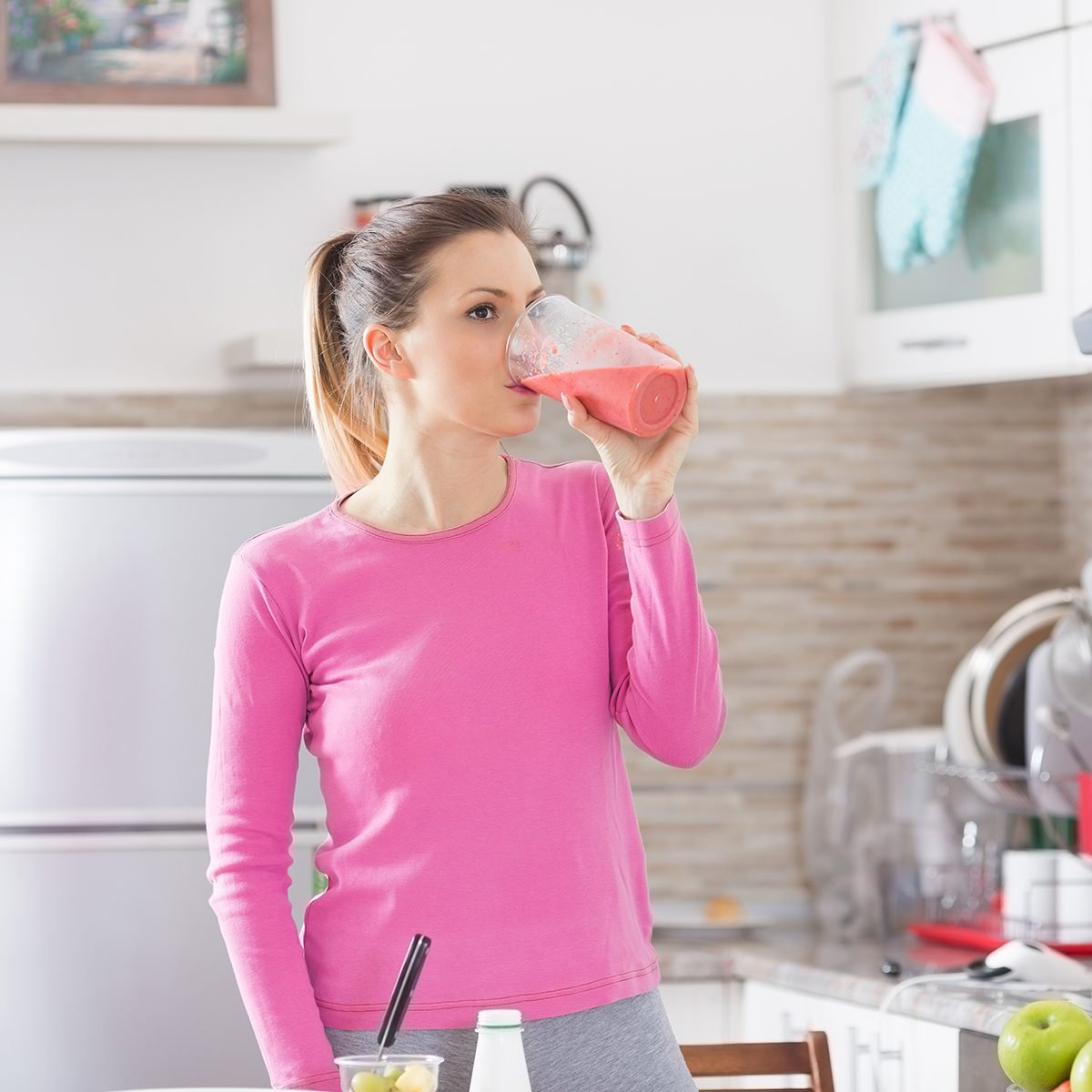 Healthy young woman drinking a fruit smoothie in her kitchen.