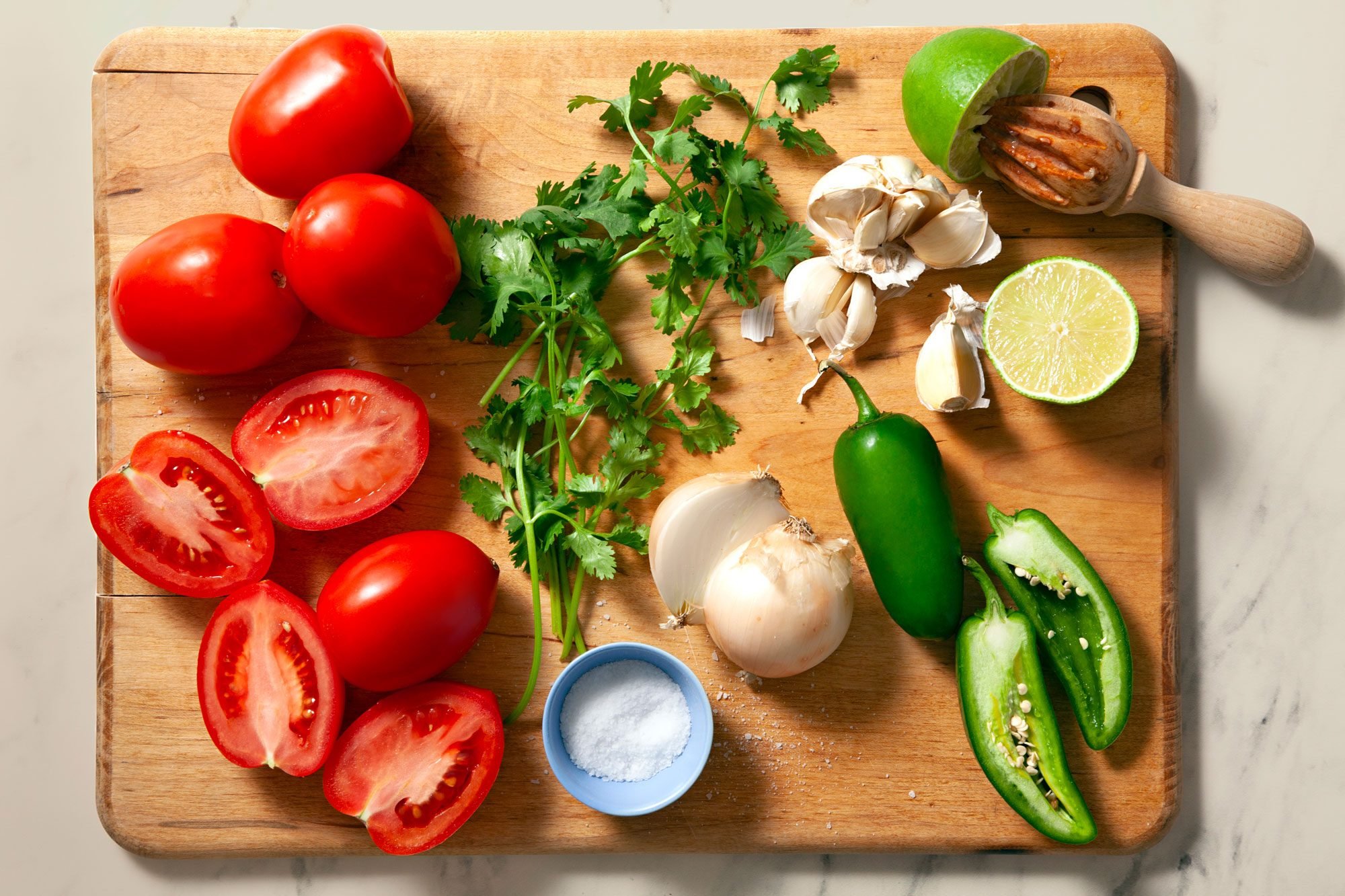 Overhead shot of all ingredients for pico de gallo; wooden chopping board; marble background;