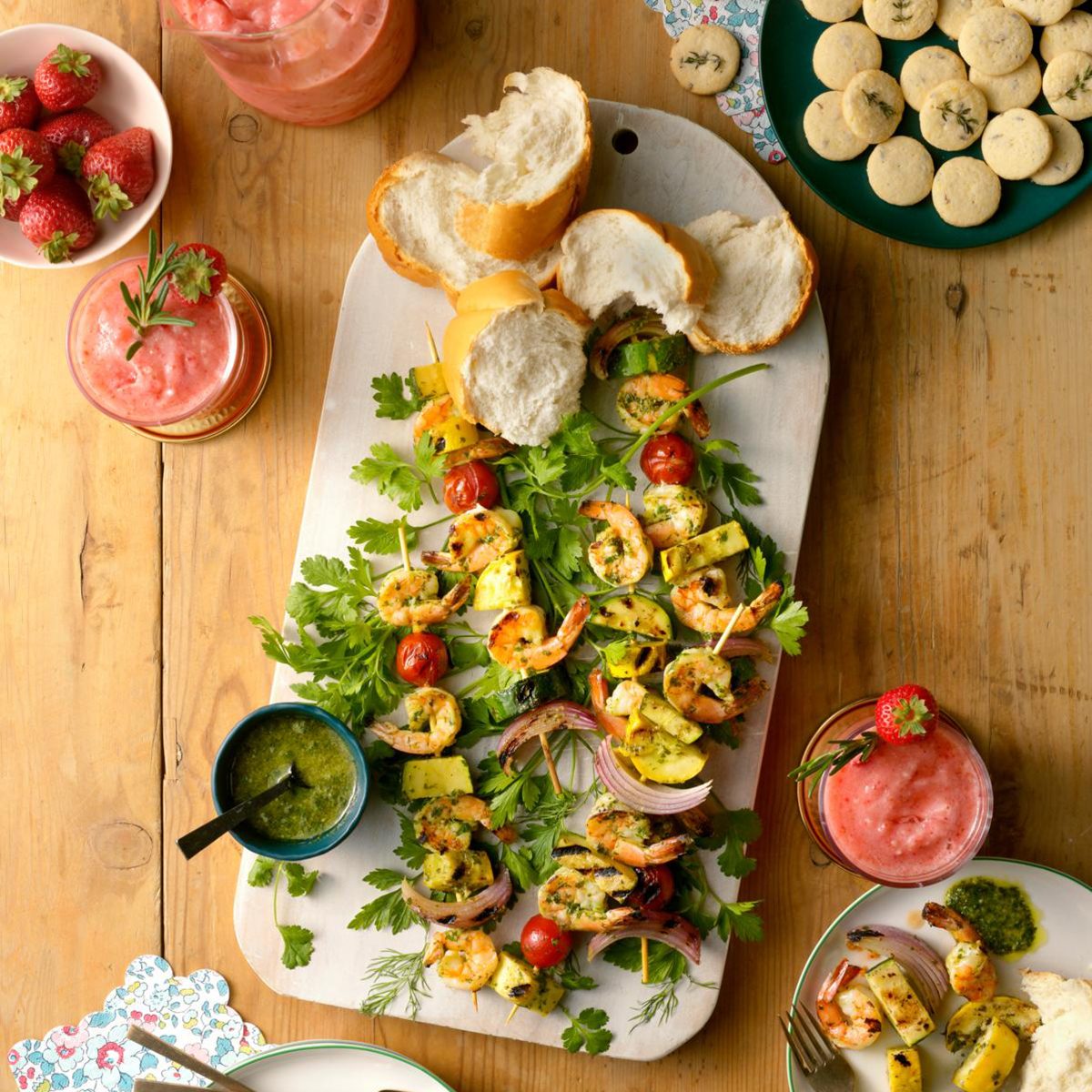 shrimp and vegetable skwers on platter with strawberry drinks cookies and bread