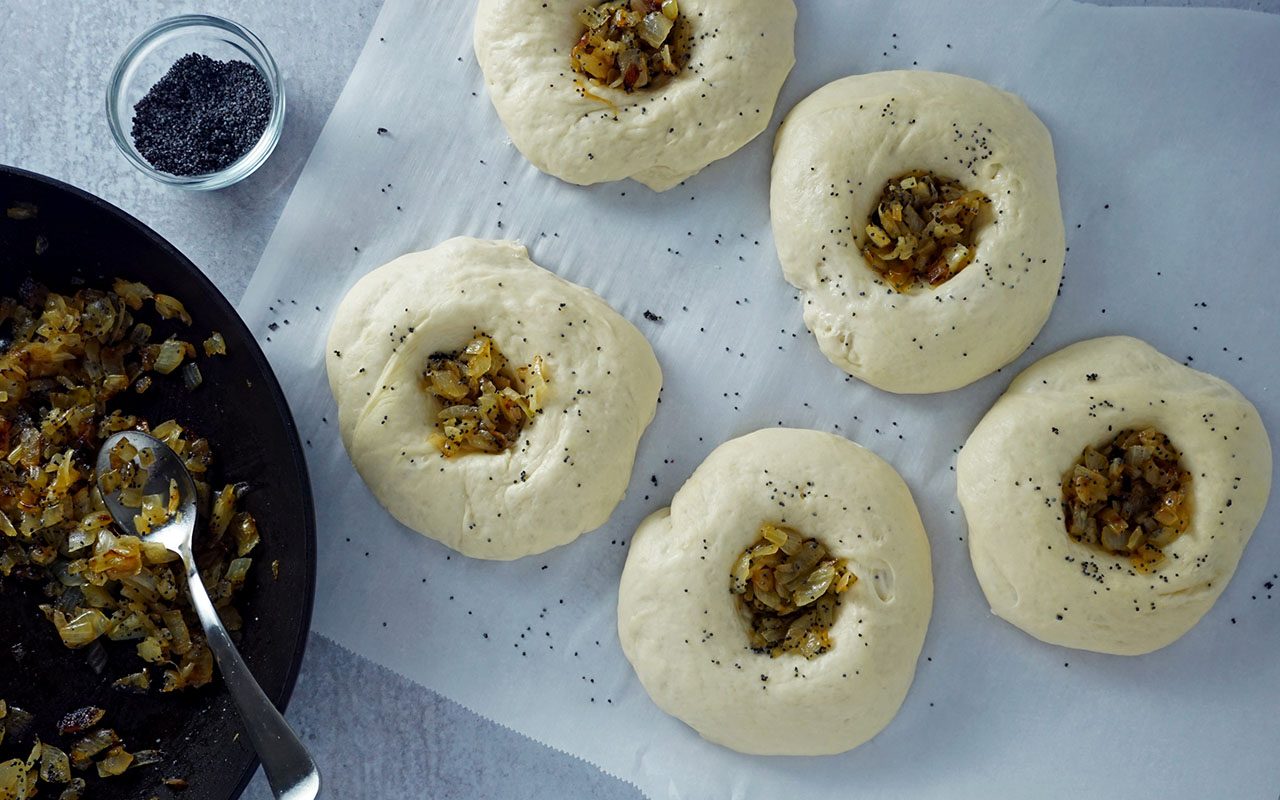 Bialy-Teig geformt, mit Zwiebeln gefüllt und bereit zum Backen