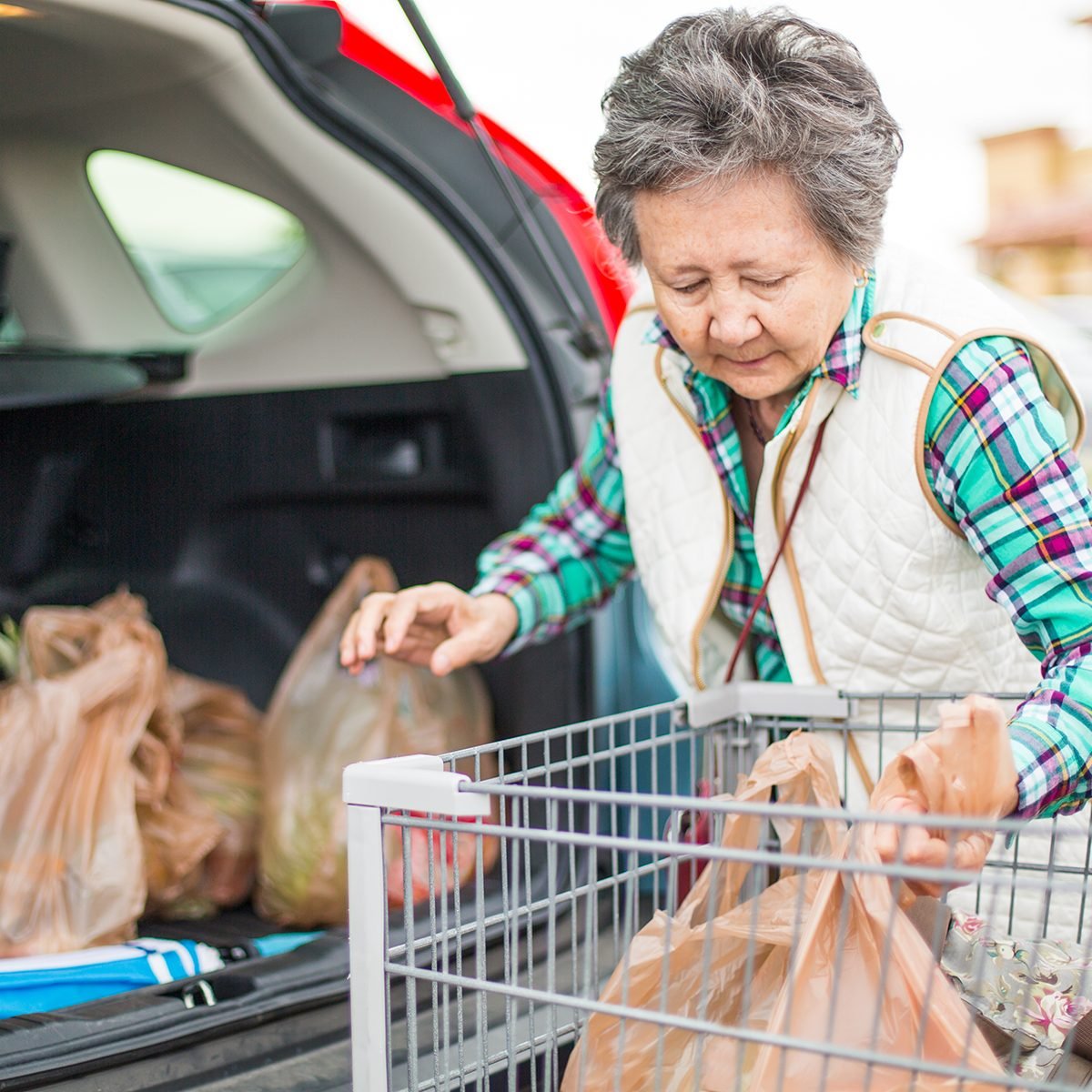 Senior woman loading grocery bags in the trunk of her car.