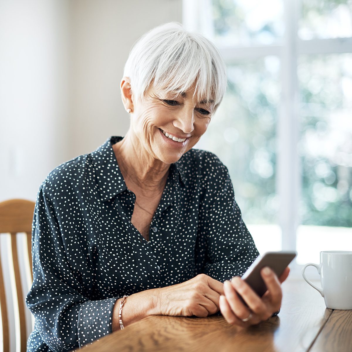 Cropped shot a senior woman sending a text while sitting in her living room at home