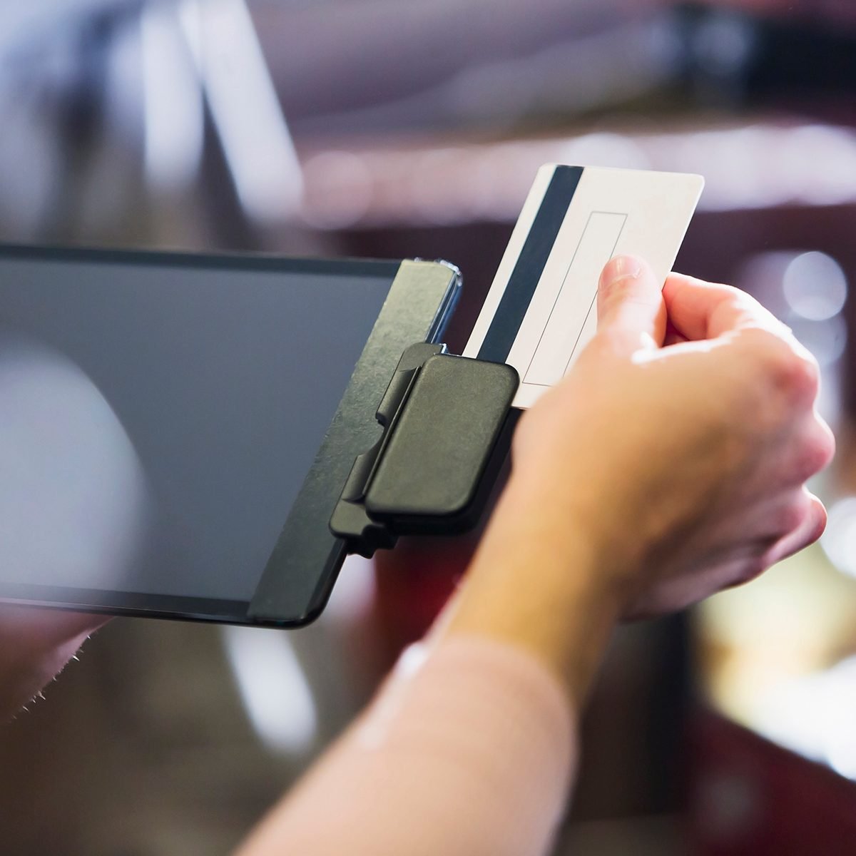 Close up of a female hand swiping a credit card or gift card through a reader attached to a digital tablet.