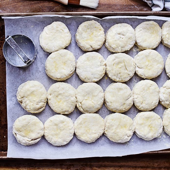 Raw buttermilk southern biscuit or scone dough from scratch with egg brush washed on arranged with rolling pin, biscuit cutter and basting brush. Top view.