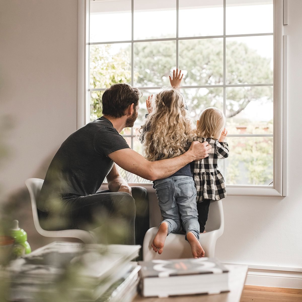 Father and two small kids looking out a window together