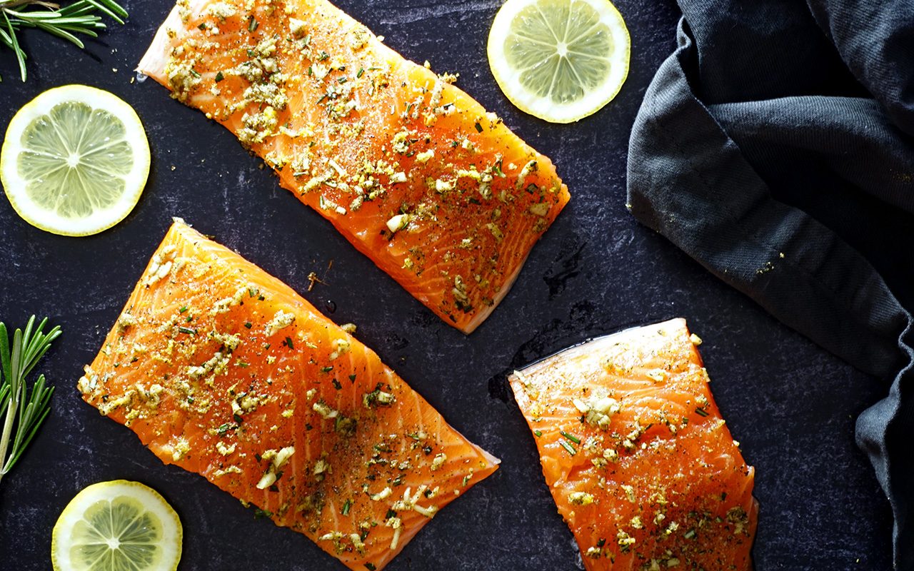 raw salmon filets with a lemon rosemary rub applied to their flesh on a slate background