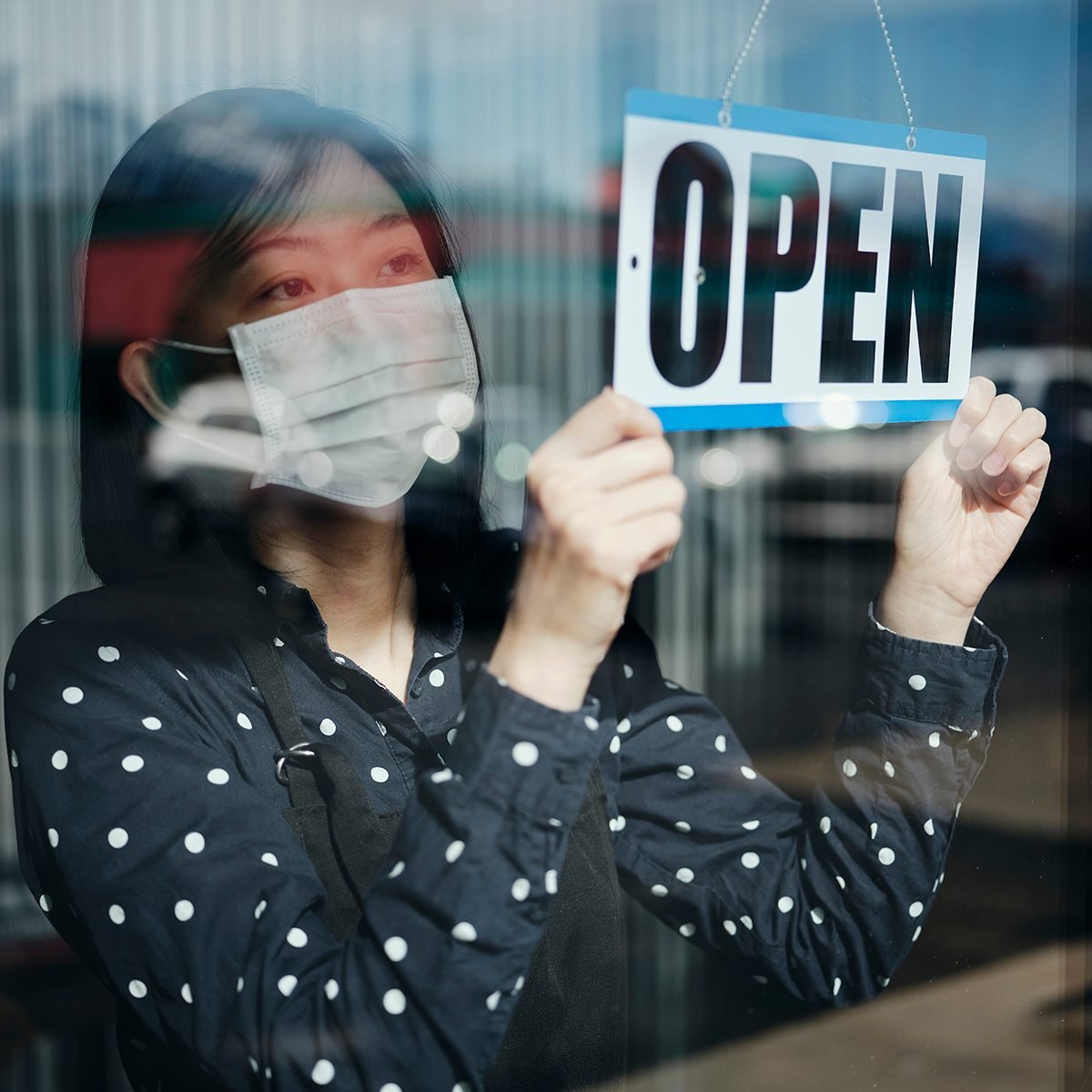 A business owner changing the store sign to OPEN after being closed for a period of time due to social distancing guidelines related to Coronavirus.