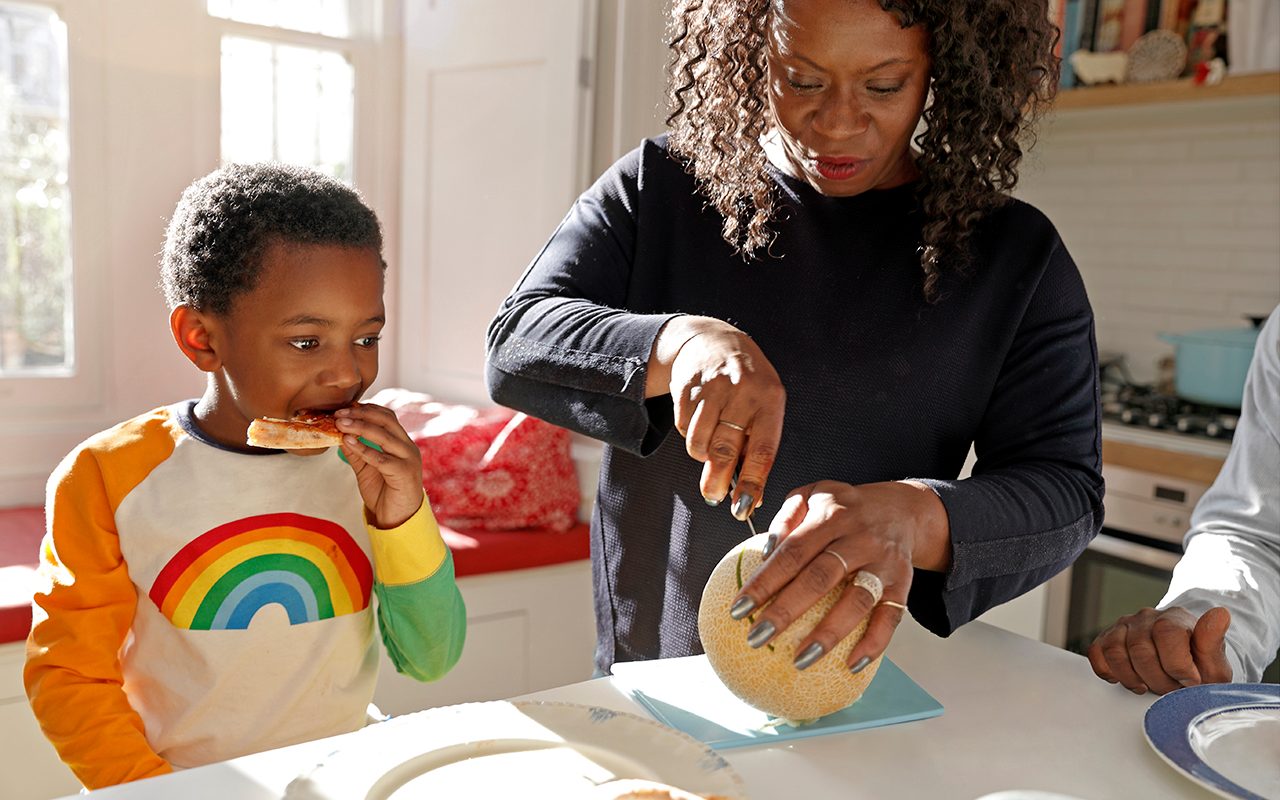 Mother cutting her young son some melon at home in the kitchen