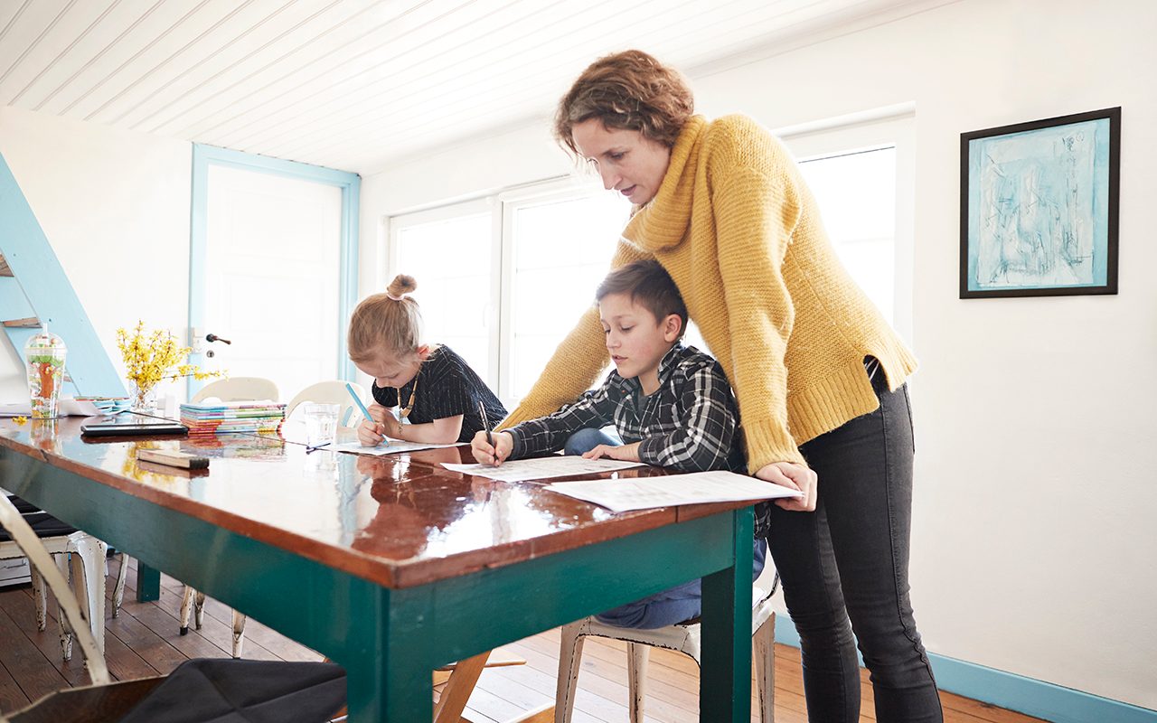 Mother homeschooling daughter and son at dining table