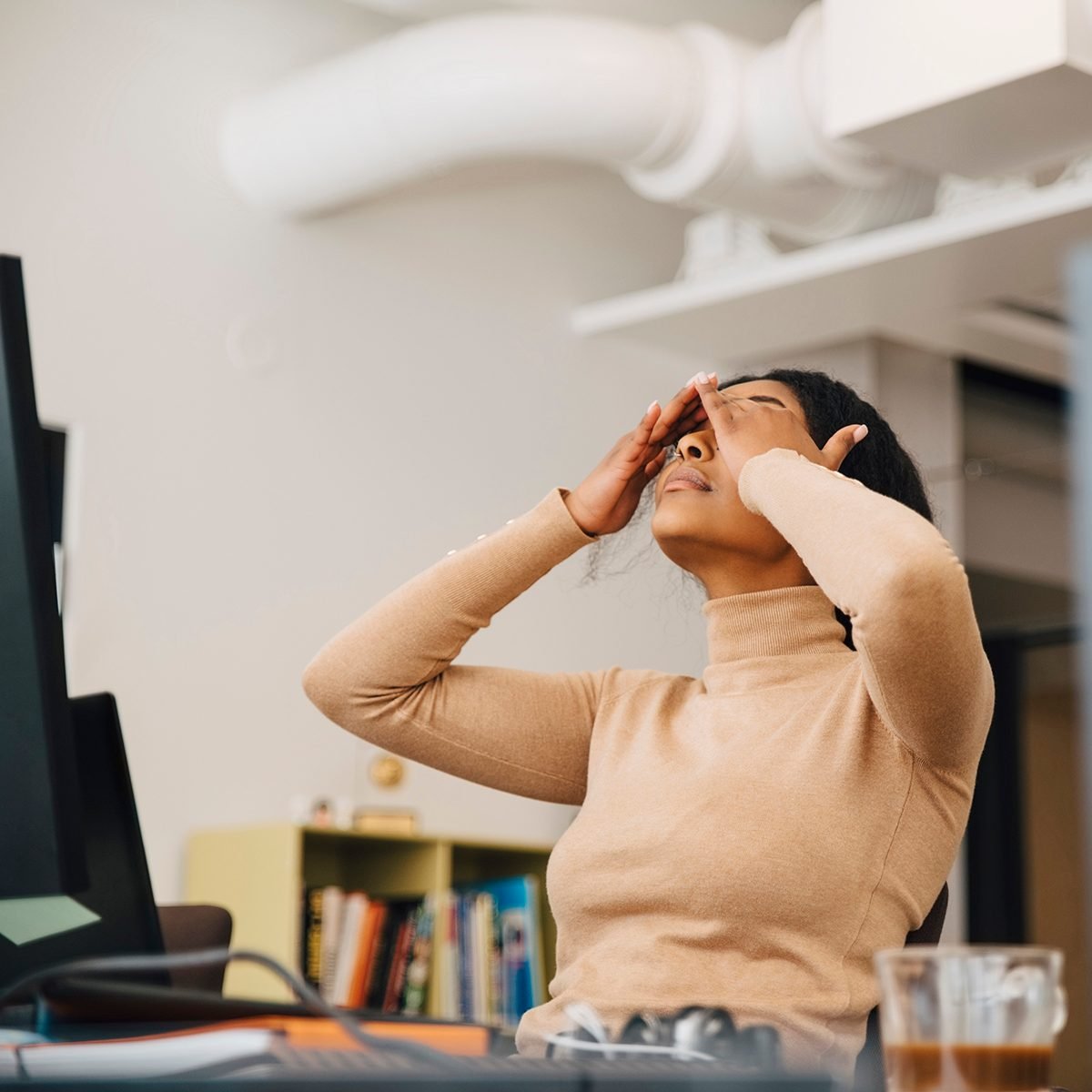 Frustrated female computer programmer with head in hands sitting in creative office