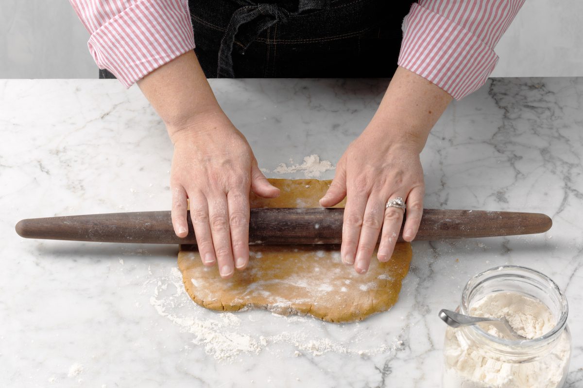 Hands rolling out cookie dough in order to make cutout cookies.