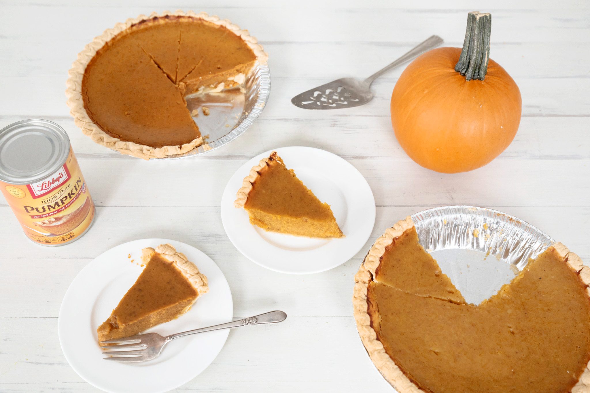 two different pumpkin pies in pie dishes with slices missing and two smaller plates with a slice of pumpkin pie