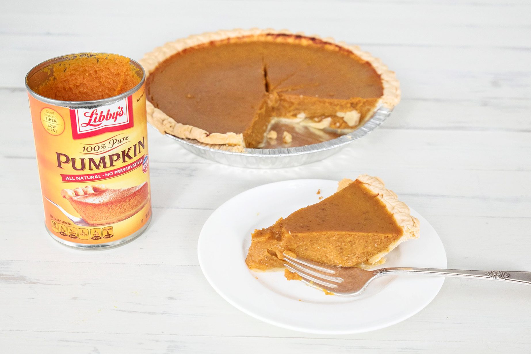 a can of libby's pumpkin, a pumpkin pie in pie dish with a slice missing, and a slice of pie on a white plate with a fork