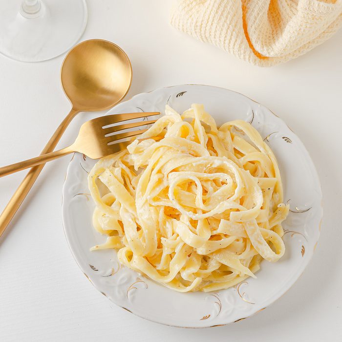 Conventional Italian Pasta Fetuccini Alfredo On A White Table With Golden Appliances