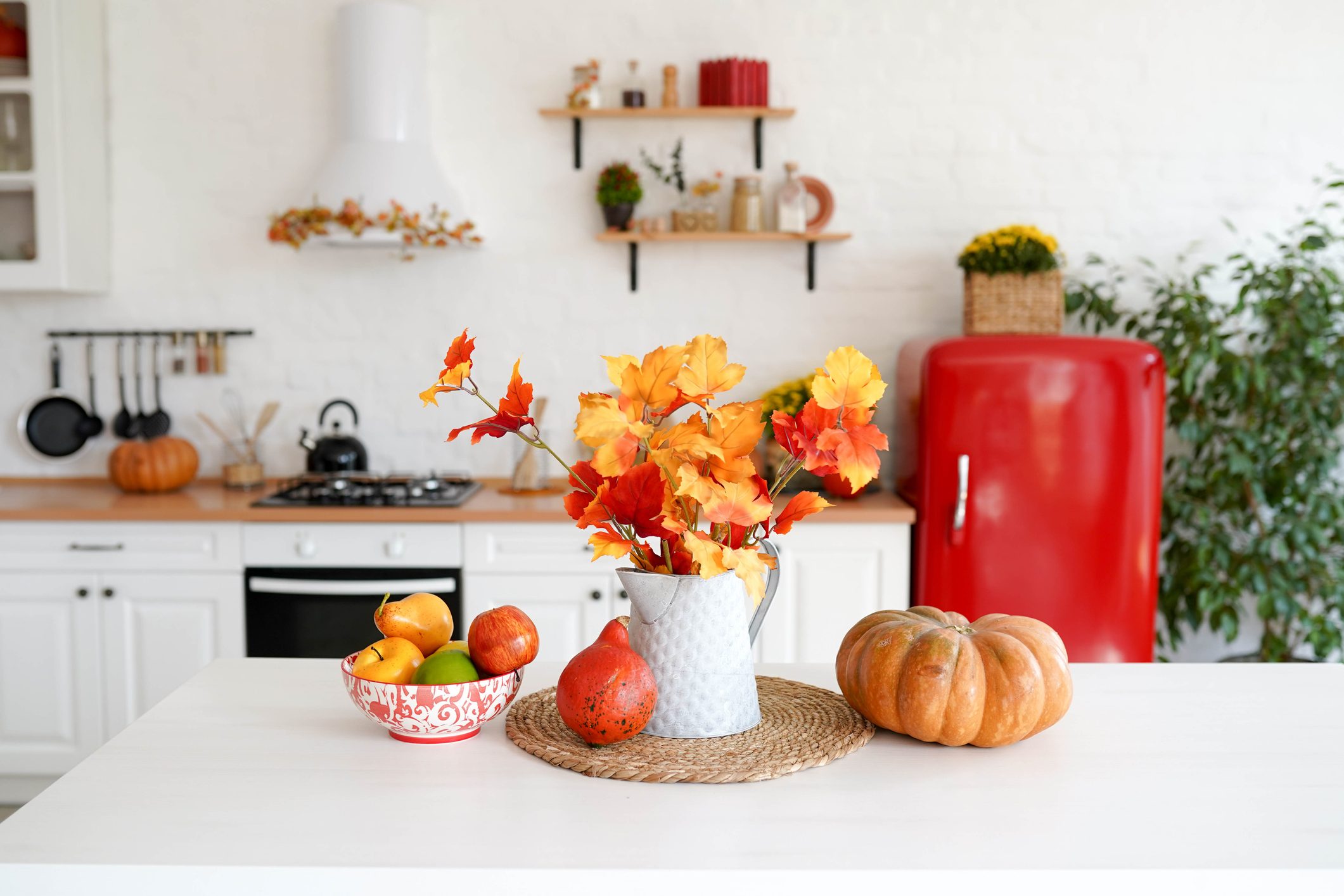 autumn table with vegetables and autumn decor in kitchen. red and yellow leaves in the vase and pumpkin on white background.