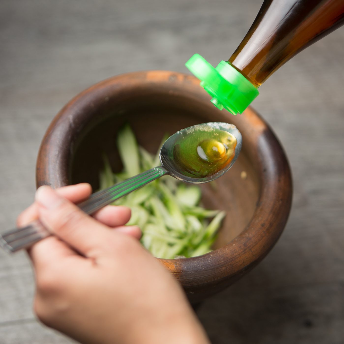 pouring fish sauce from bottle onto spoon while cooking