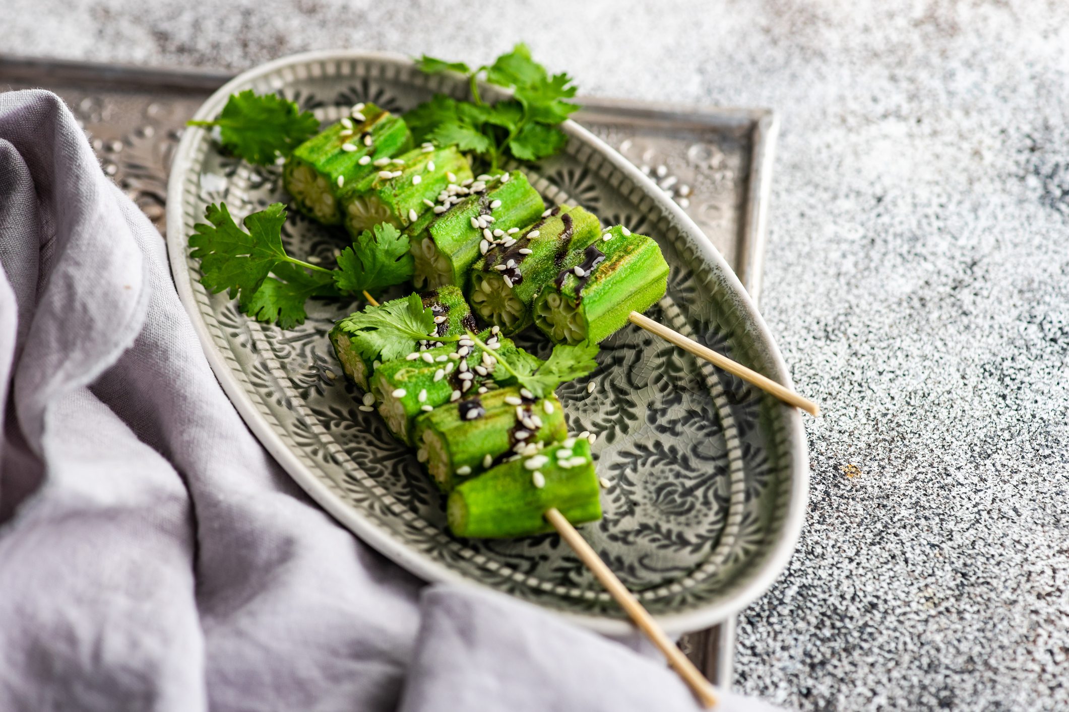 Overhead view of barbecue skewers of chopped okra with sesame seeds, coriander and soy sauce on a plate