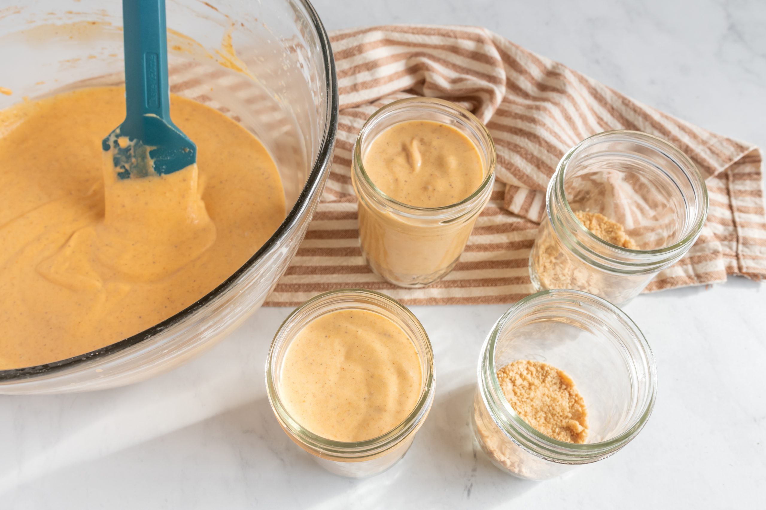 No-Bake Pumpkin Cheesecakes Being Spooned into Mini Jars