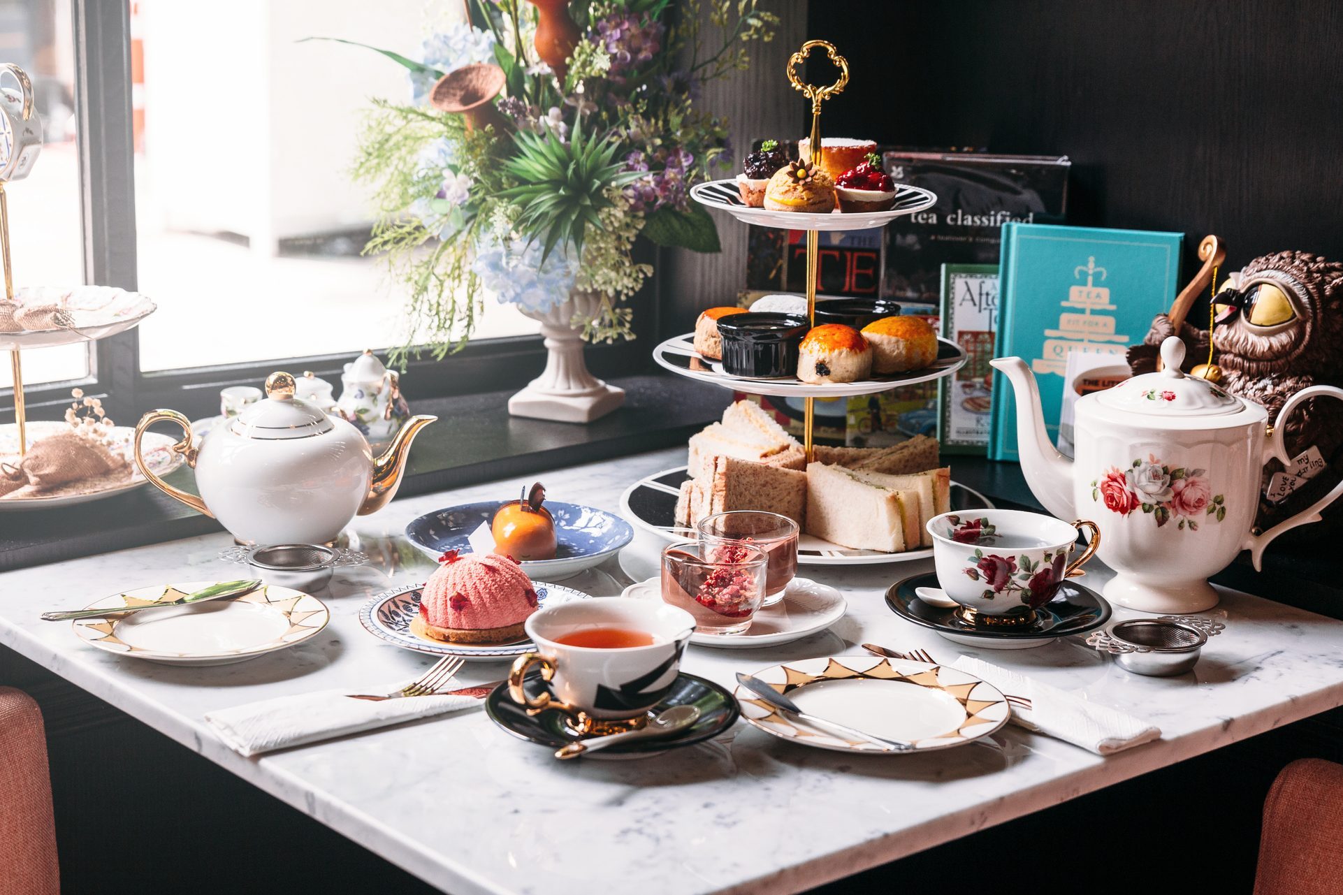 English afternoon tea set including hot tea, pastry, scones, sandwiches and mini pies on marble top table.