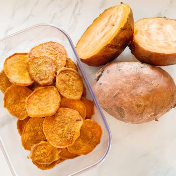 sweet potato dog treats in a container next to raw sweet potatoes