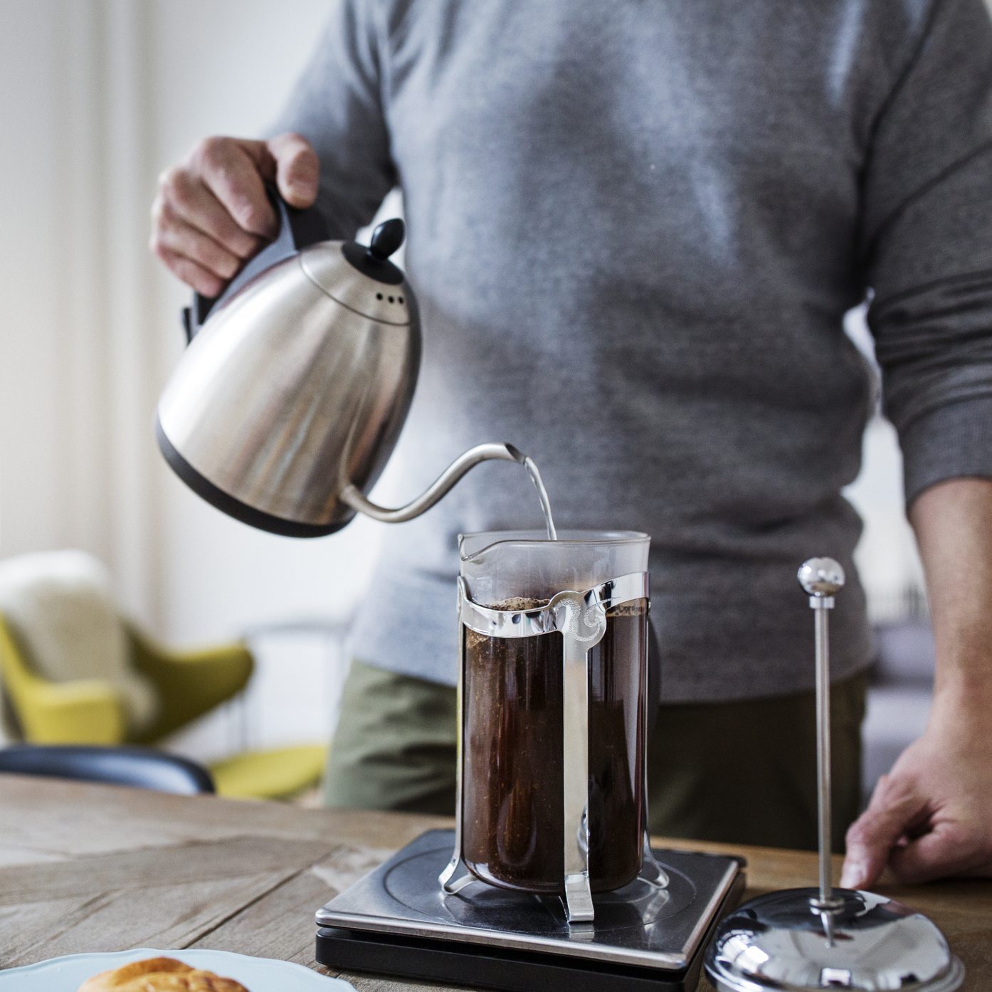 Midsection of man pouring water in French press while preparing coffee at home