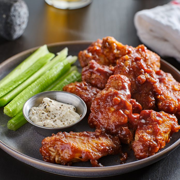 boneless chicken wings covered in honey garlic bbq sauce with ranch and celery on a table with a beer out of focus