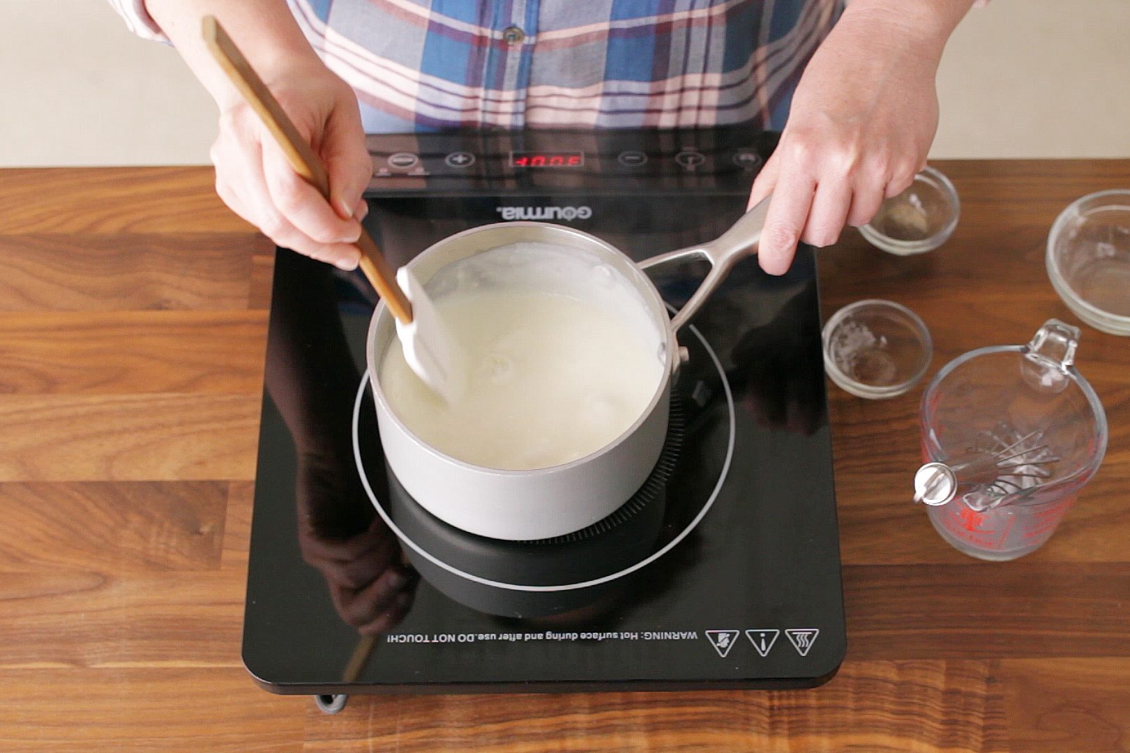 top view of pot on a stove and hands staring the white sauce with a rubber spatula
