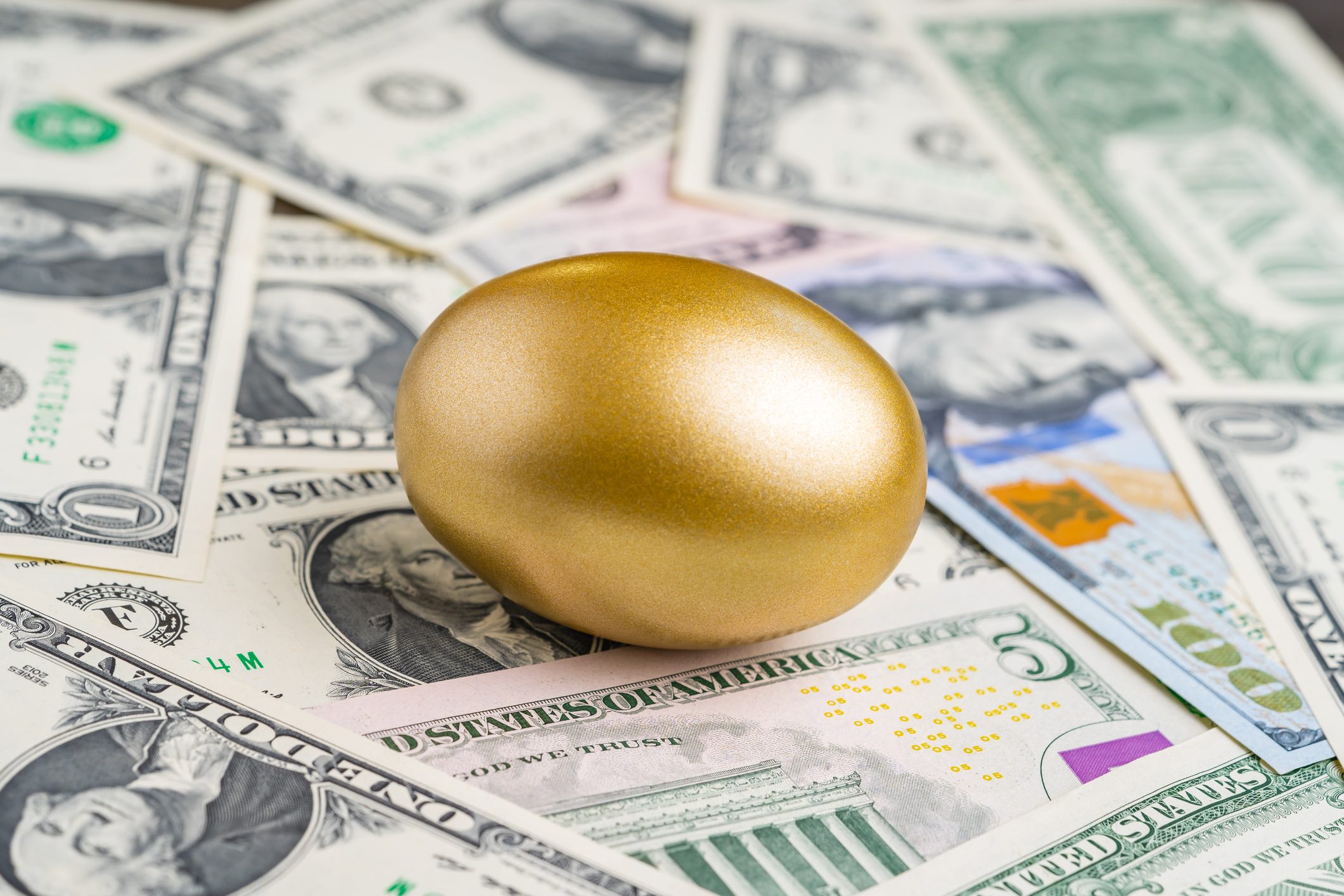 Shiny golden egg on pile of US America dollar banknotes for Easter egg hunt