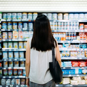 Rear view of young Asian mother groceries shopping for baby products in a supermarket