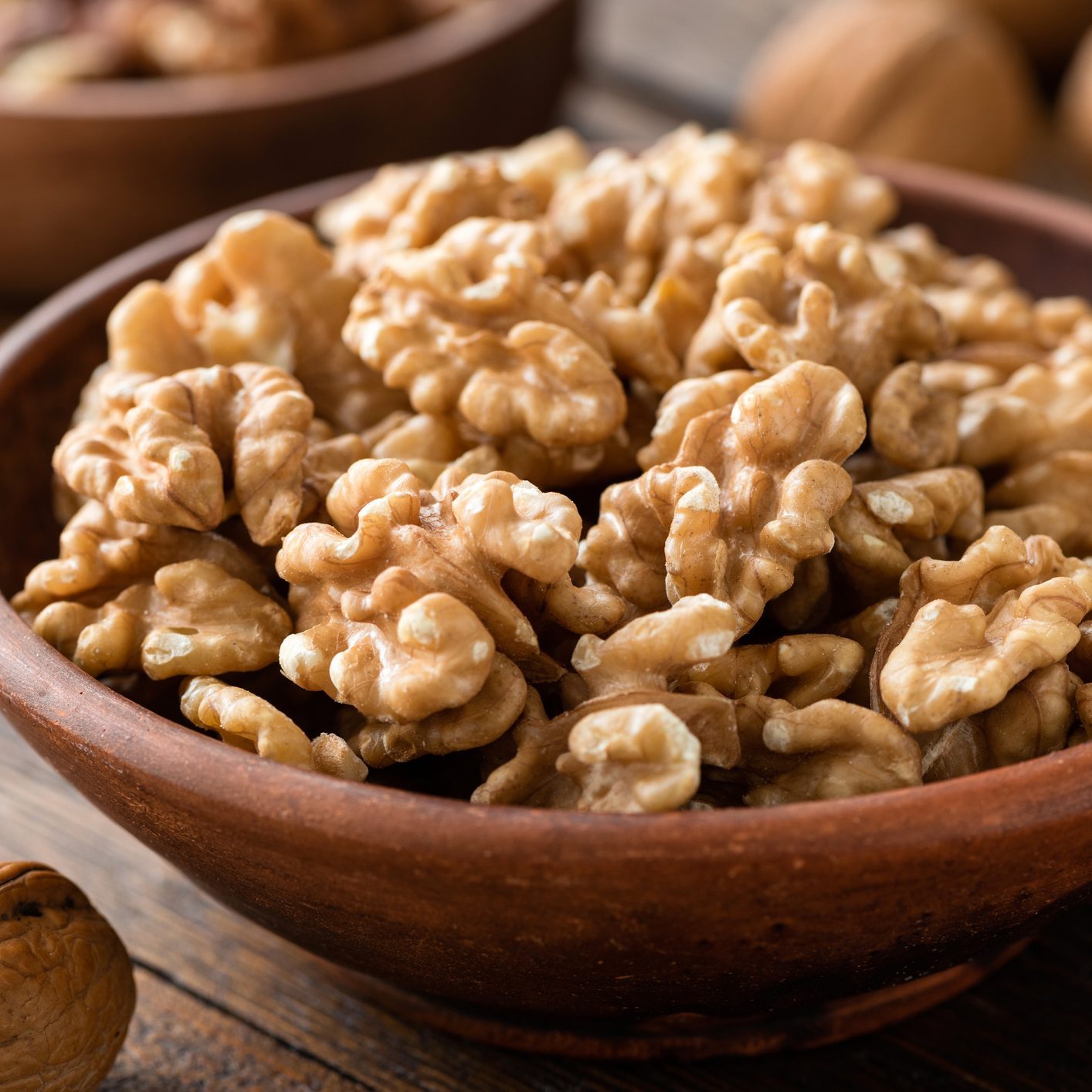 Walnuts in brown bowl on wooden table